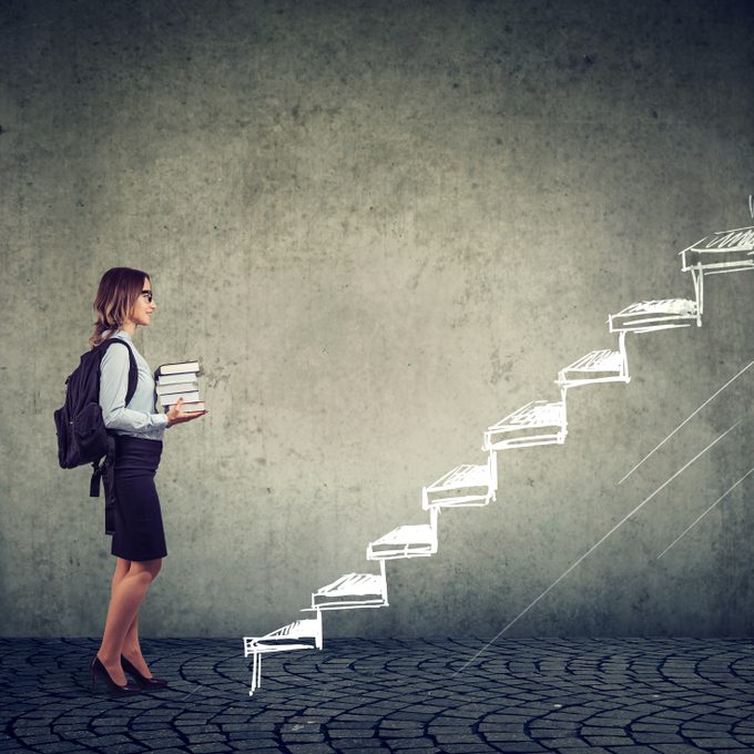 Female,Student,With,Books,Standing,On,The,Stairs,Of,Education