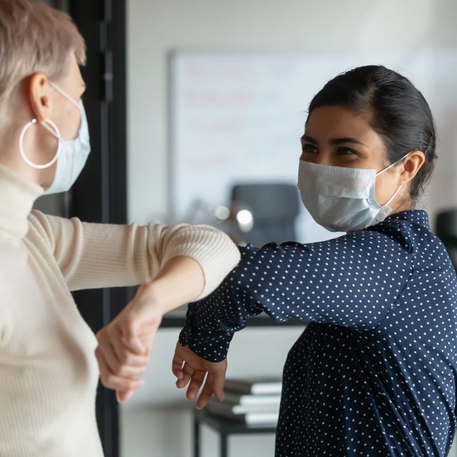 Smiling,Diverse,Female,Colleagues,Wearing,Protective,Face,Masks,Greeting,Bumping